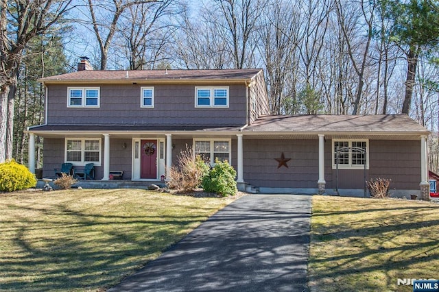 view of front of home featuring a front yard, a porch, driveway, and a chimney