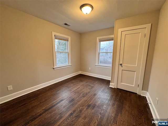 empty room with dark wood-style floors, visible vents, and baseboards