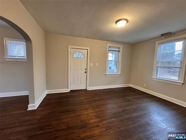 entryway with arched walkways, dark wood-style flooring, and baseboards