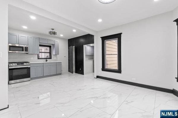 kitchen with marble finish floor, stainless steel appliances, tasteful backsplash, gray cabinetry, and baseboards