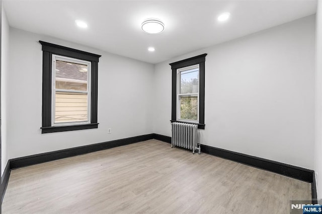 spare room with radiator heating unit, baseboards, wood finished floors, and recessed lighting