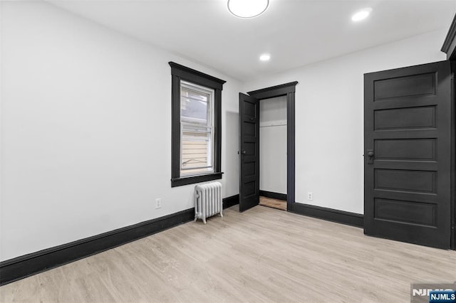 unfurnished bedroom with light wood-type flooring, baseboards, radiator heating unit, and recessed lighting