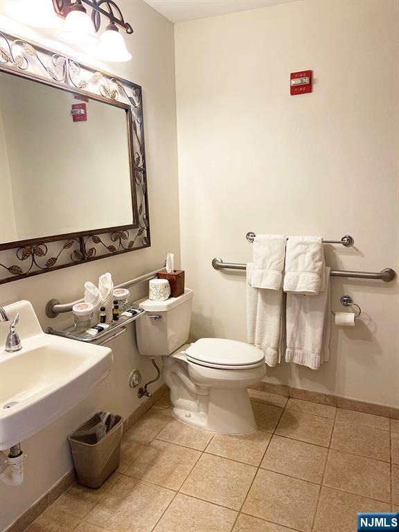 half bathroom with a sink, tile patterned flooring, toilet, and baseboards