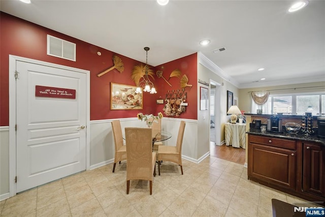 dining room with a wainscoted wall, visible vents, crown molding, and a notable chandelier