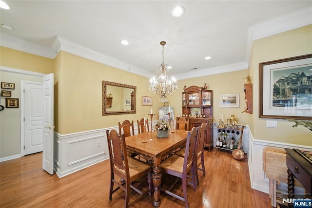 dining space featuring light wood-style floors, wainscoting, crown molding, and a notable chandelier