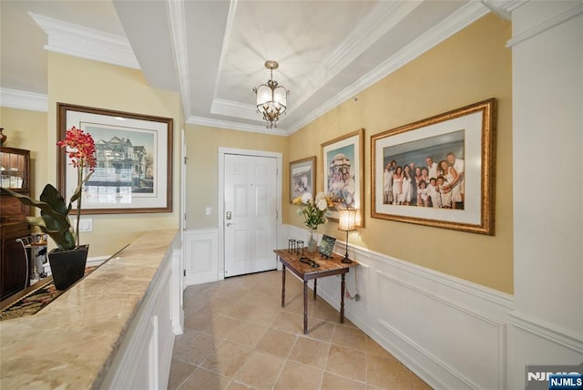 entryway with a wainscoted wall, a tray ceiling, a chandelier, and crown molding