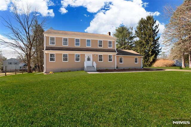 view of front facade featuring a chimney, fence, and a front lawn