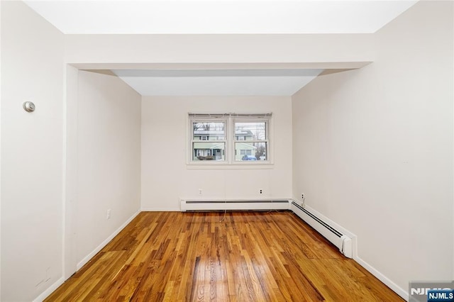 empty room featuring baseboard heating, wood finished floors, and baseboards