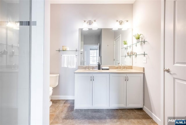 bathroom featuring toilet, double vanity, baseboards, and a sink