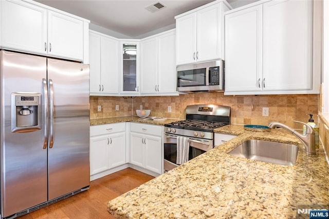 kitchen with a sink, visible vents, appliances with stainless steel finishes, tasteful backsplash, and glass insert cabinets