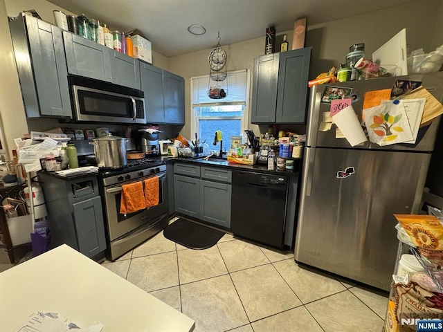 kitchen featuring light tile patterned floors, stainless steel appliances, dark countertops, gray cabinets, and a sink