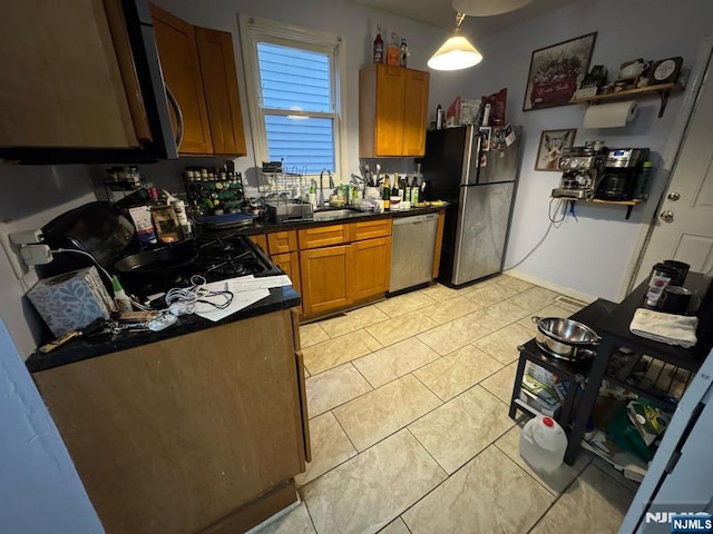 kitchen featuring light tile patterned floors, dark countertops, appliances with stainless steel finishes, brown cabinetry, and a sink