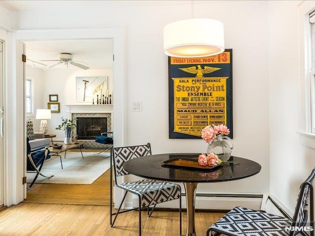 dining space with light wood-style floors, ceiling fan, and a tiled fireplace