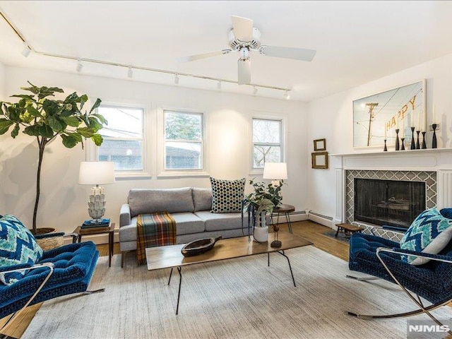 living room featuring a baseboard heating unit, a fireplace, ceiling fan, and wood finished floors