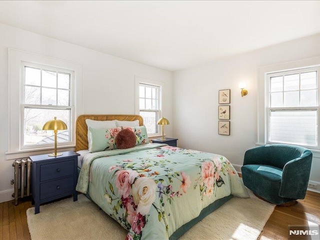 bedroom with baseboards, radiator heating unit, and light wood-style floors