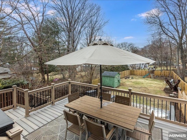 deck with a fenced backyard, an outbuilding, a shed, a playground, and outdoor dining space