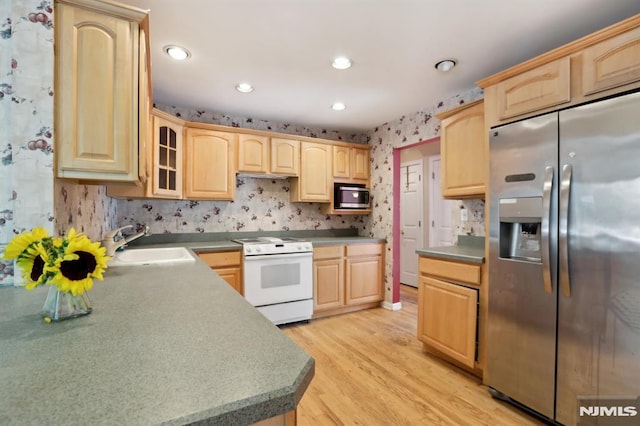 kitchen with light brown cabinets, wallpapered walls, glass insert cabinets, appliances with stainless steel finishes, and a sink