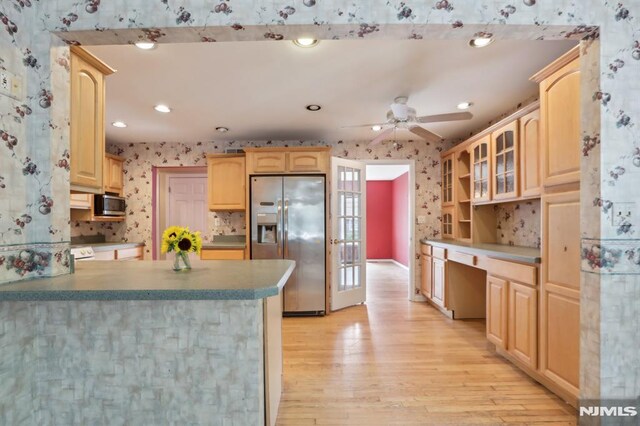 kitchen featuring light brown cabinetry, a peninsula, appliances with stainless steel finishes, wallpapered walls, and built in study area