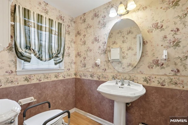 half bathroom featuring wallpapered walls, toilet, wood finished floors, and baseboards