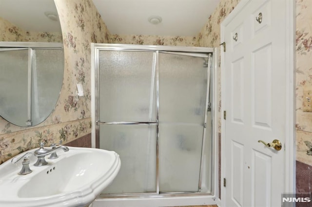 full bath featuring wallpapered walls, a shower stall, and a sink