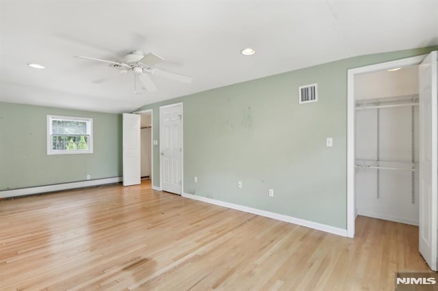 unfurnished bedroom with visible vents, a walk in closet, light wood-style flooring, baseboards, and baseboard heating