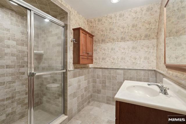 full bathroom featuring vanity, wallpapered walls, a stall shower, wainscoting, and tile walls