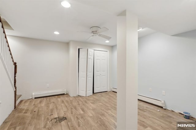 below grade area featuring stairs, light wood-type flooring, baseboard heating, and a baseboard radiator