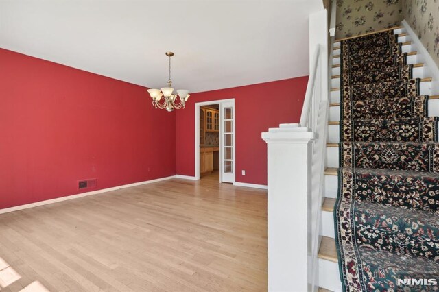 staircase with visible vents, baseboards, an inviting chandelier, and wood finished floors