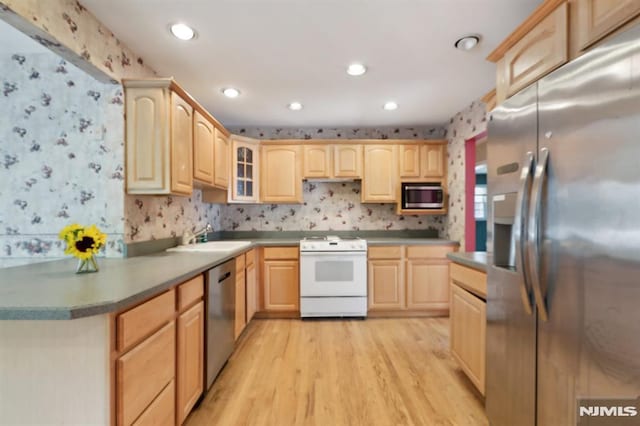 kitchen featuring light wood-style flooring, light brown cabinets, a sink, appliances with stainless steel finishes, and wallpapered walls