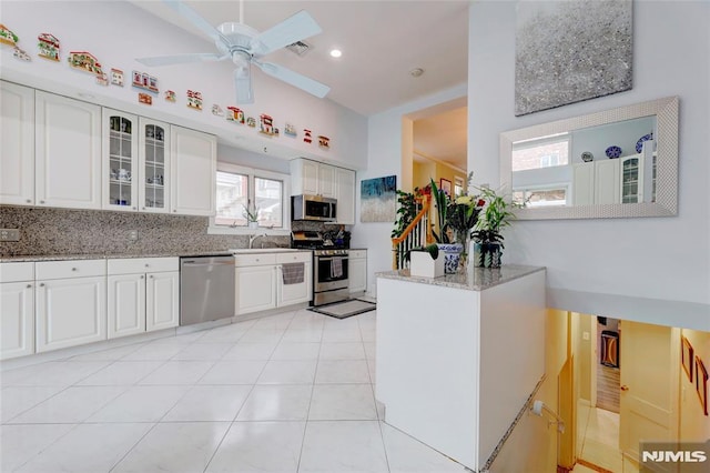 kitchen with glass insert cabinets, light stone countertops, stainless steel appliances, backsplash, and light tile patterned flooring