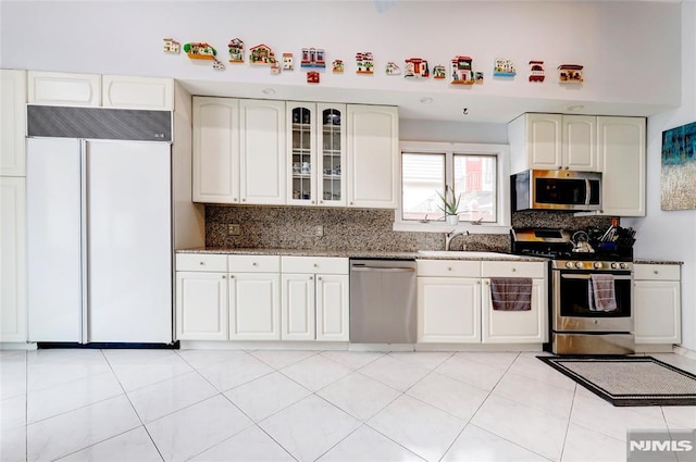 kitchen with dark stone counters, decorative backsplash, glass insert cabinets, stainless steel appliances, and white cabinetry