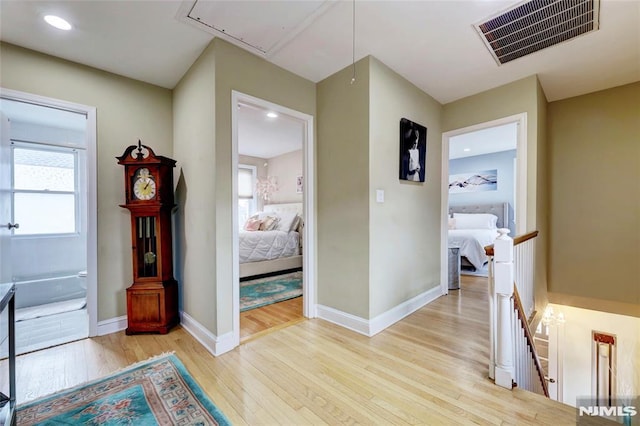 corridor with light wood-style flooring, visible vents, baseboards, an upstairs landing, and attic access