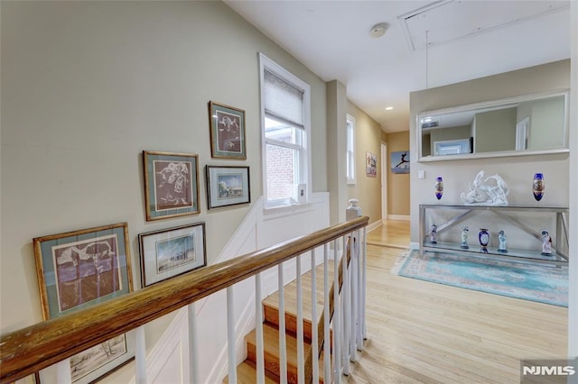 hall with light wood finished floors, an upstairs landing, attic access, and baseboards