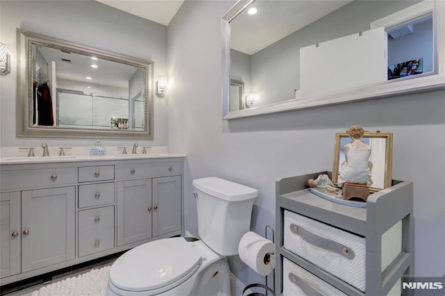 bathroom with toilet, double vanity, walk in shower, and a sink