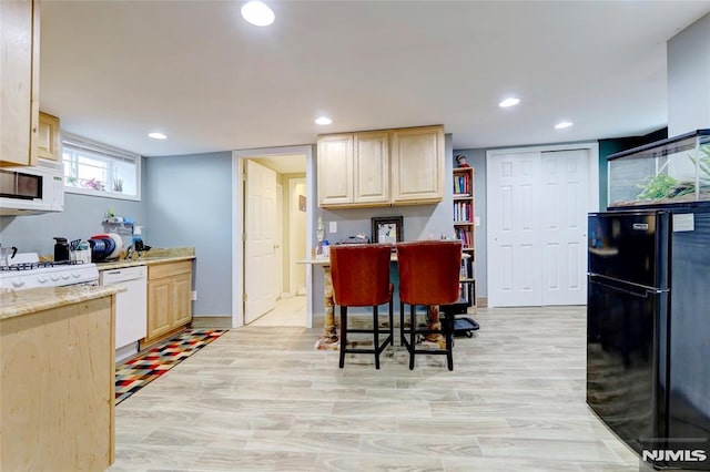 kitchen featuring light brown cabinetry, white appliances, light stone counters, and recessed lighting