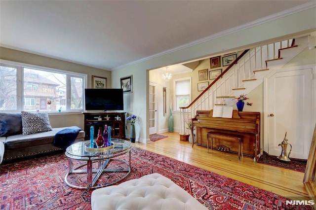 living room featuring crown molding, wood finished floors, baseboards, stairway, and an inviting chandelier