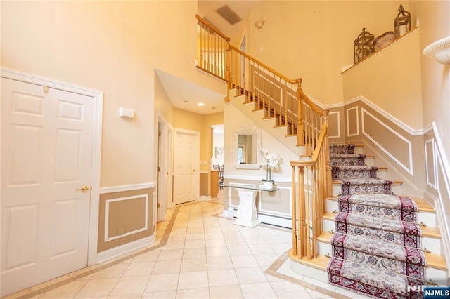 stairs with tile patterned flooring, visible vents, wainscoting, a high ceiling, and a decorative wall