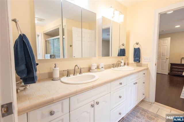 bathroom with a sink, a shower with door, double vanity, and tile patterned floors