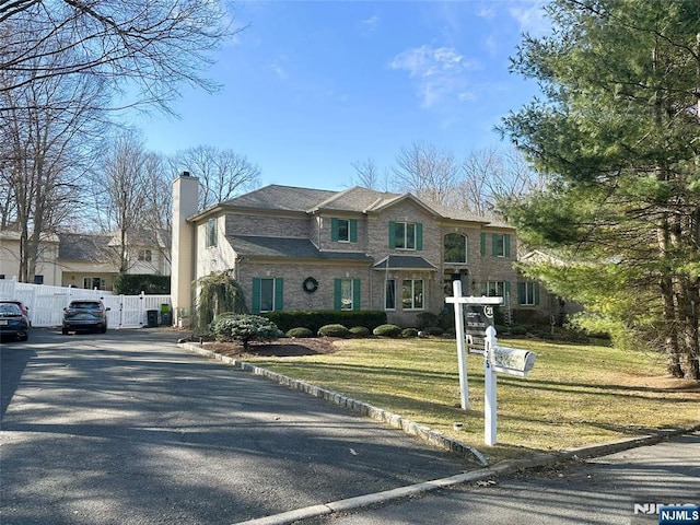 view of front of property featuring brick siding, a front lawn, fence, aphalt driveway, and a chimney