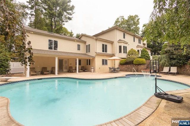 outdoor pool with a patio, fence, and a diving board