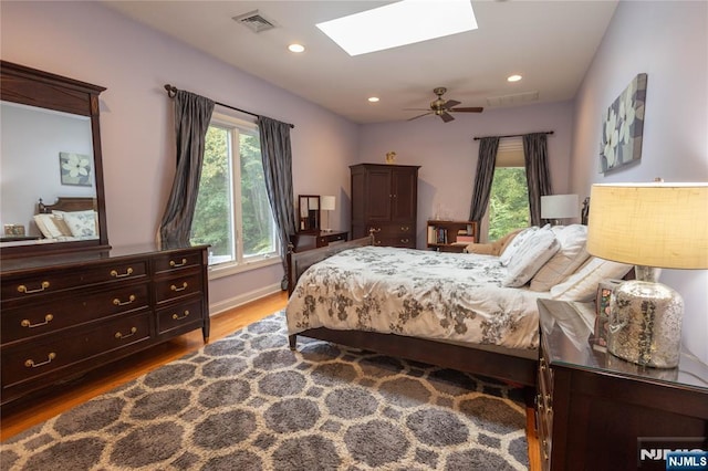 bedroom with a ceiling fan, wood finished floors, visible vents, a skylight, and recessed lighting