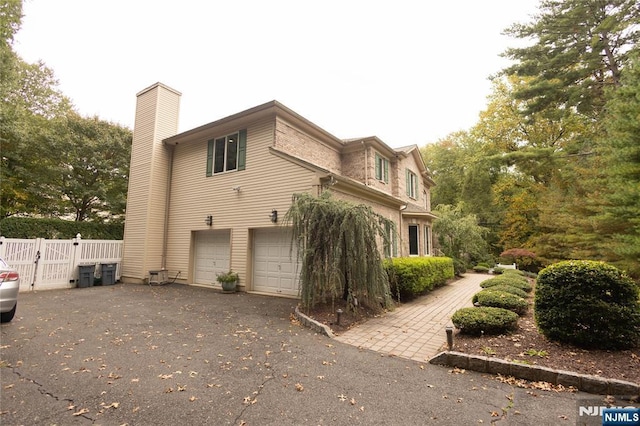 view of side of property with a gate, aphalt driveway, fence, a garage, and a chimney