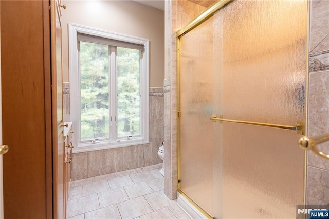 bathroom with tile patterned floors, a shower stall, toilet, and tile walls