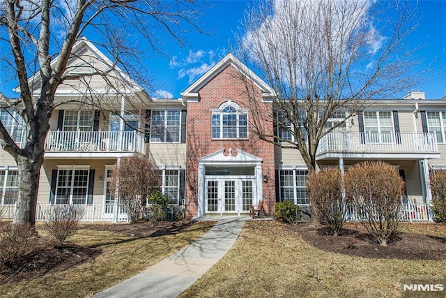 view of front of house featuring french doors, a front lawn, brick siding, and a balcony