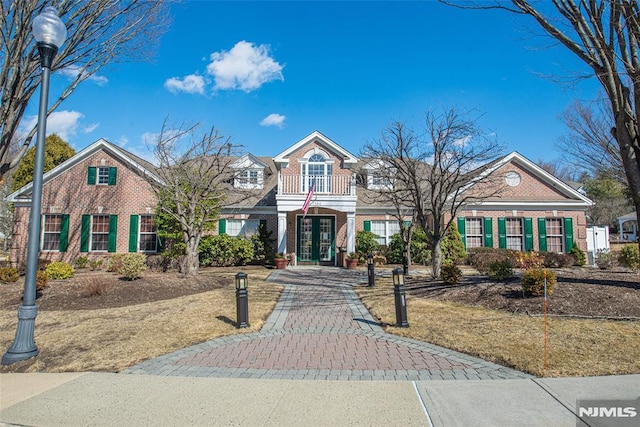 view of front of property featuring french doors, brick siding, and a balcony