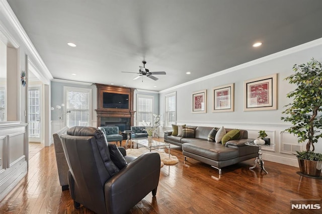 living area with a large fireplace, hardwood / wood-style flooring, a wainscoted wall, crown molding, and a decorative wall