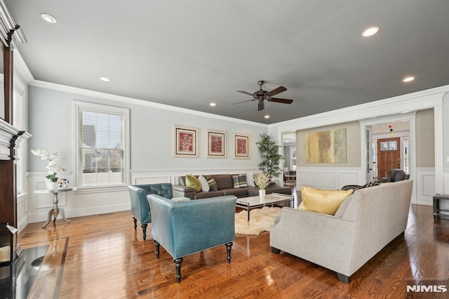 living room with ceiling fan, a decorative wall, dark wood-type flooring, ornamental molding, and wainscoting