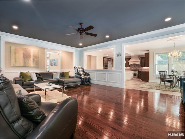 living room with a decorative wall, ceiling fan with notable chandelier, recessed lighting, wood finished floors, and crown molding