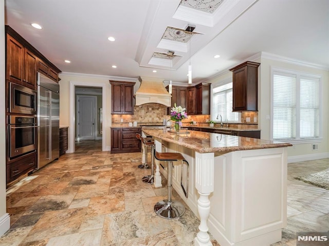 kitchen with crown molding, a breakfast bar area, custom exhaust hood, a sink, and built in appliances