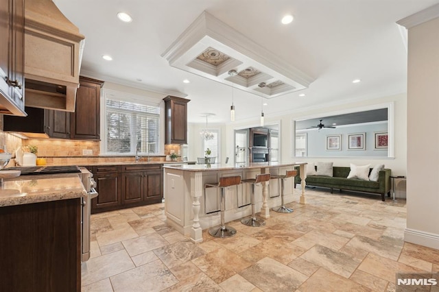 kitchen with dark brown cabinetry, a kitchen breakfast bar, open floor plan, tasteful backsplash, and crown molding